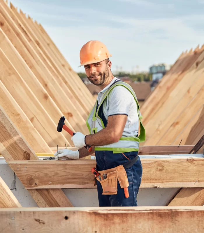 A smiling carpenter while hammering a nail of a wooden board.